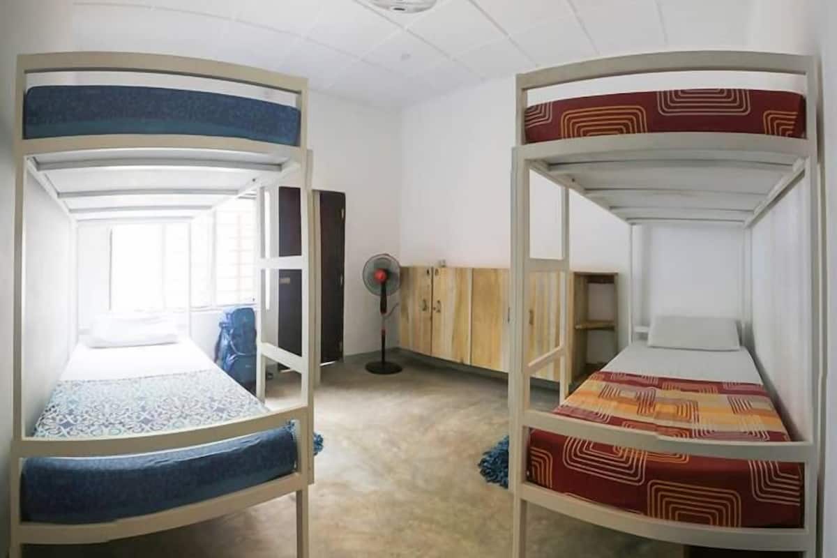 A dormitory room with bunk beds, a fan, and a window.