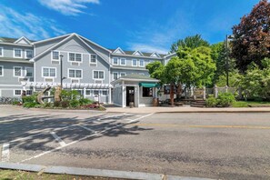 A multi-story hotel with a central entrance, a covered outdoor seating area, and a landscaped garden with a large tree. - Comfort Inn And Suites (Conway)