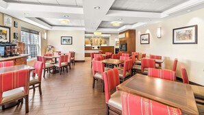 Une salle à manger d’hôtel avec de nombreuses tables et des banquettes, un espace cuisine au centre et des tableaux encadrés aux murs.