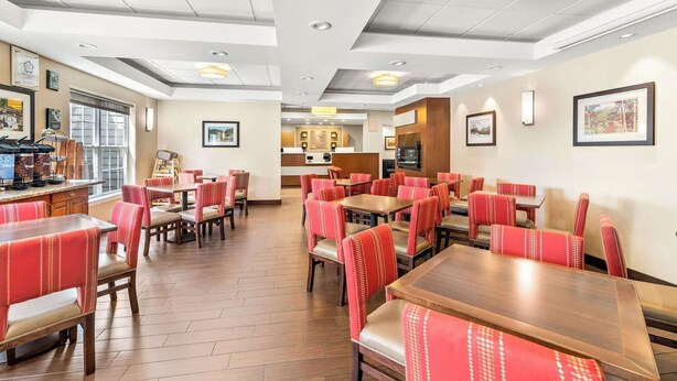 A hotel dining area with multiple tables and booths, a kitchen area in the center, and framed pictures on the walls. - Comfort Inn And Suites (Conway)