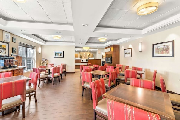 Una sala da pranzo di un hotel con diversi tavoli e cabine, una zona cucina al centro e quadri appesi alle pareti.