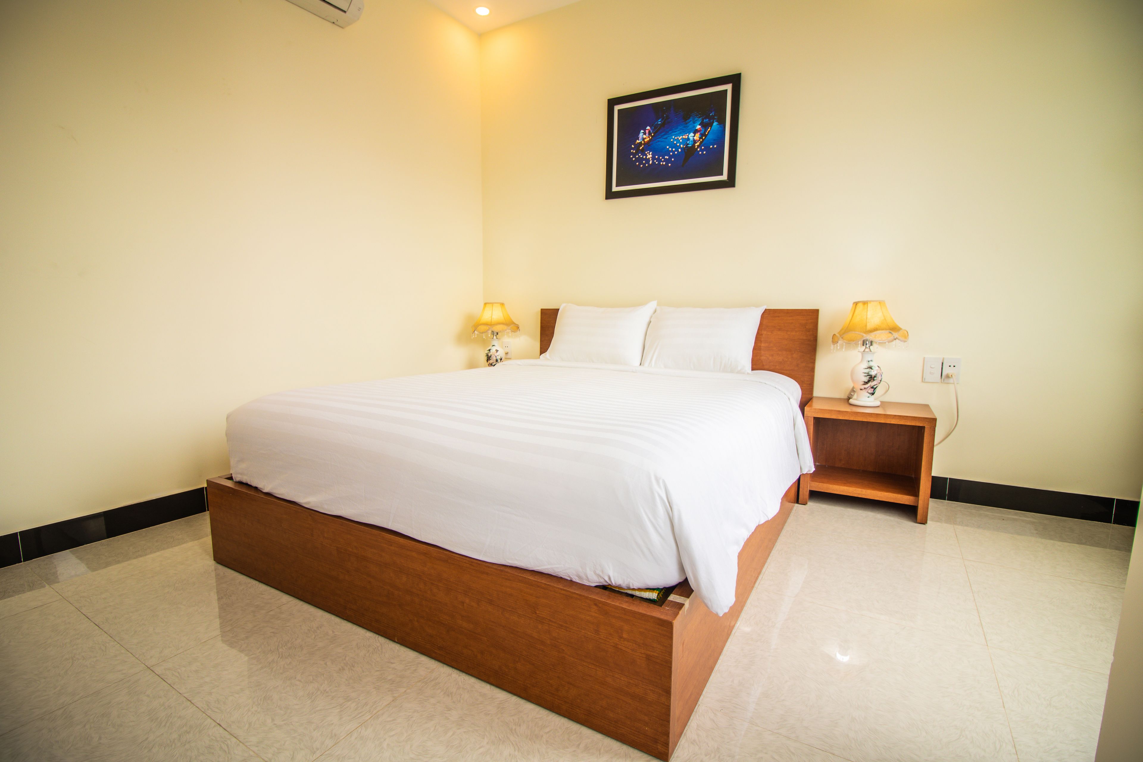A neatly made bed with white linens, a wooden headboard, and two bedside tables with lamps.