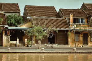 A traditional building with a tiled roof, a bicycle parked in front, and a reflection in the water. - Gold Stone Homestay Hoi An (Da Nang)