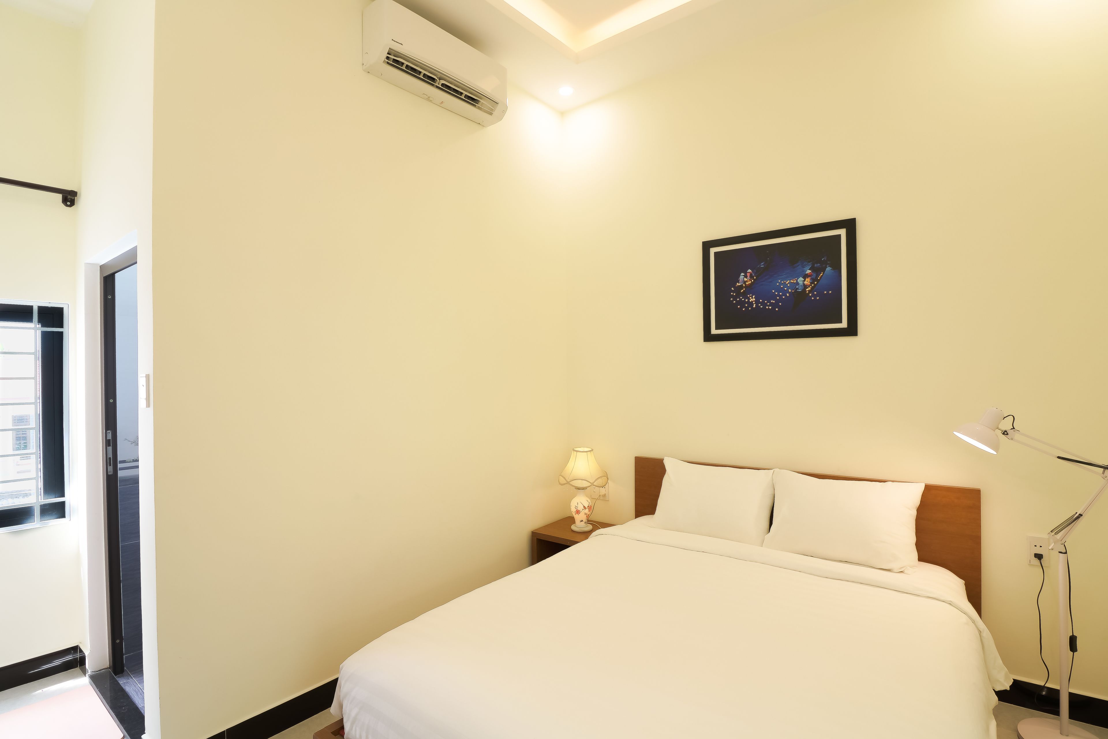 A neatly arranged hotel room with a bed, bedside lamp, and a framed picture on the wall.