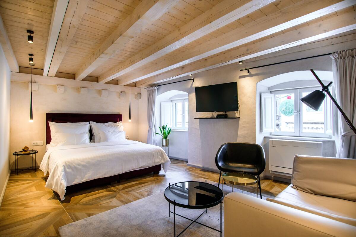 A modern bedroom with a large bed, a sofa, a small table, and a TV mounted on the wall.