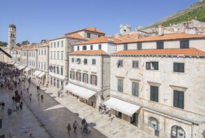 Uma rua histórica com edifícios de pedra, uma torre do relógio e um céu azul límpido.