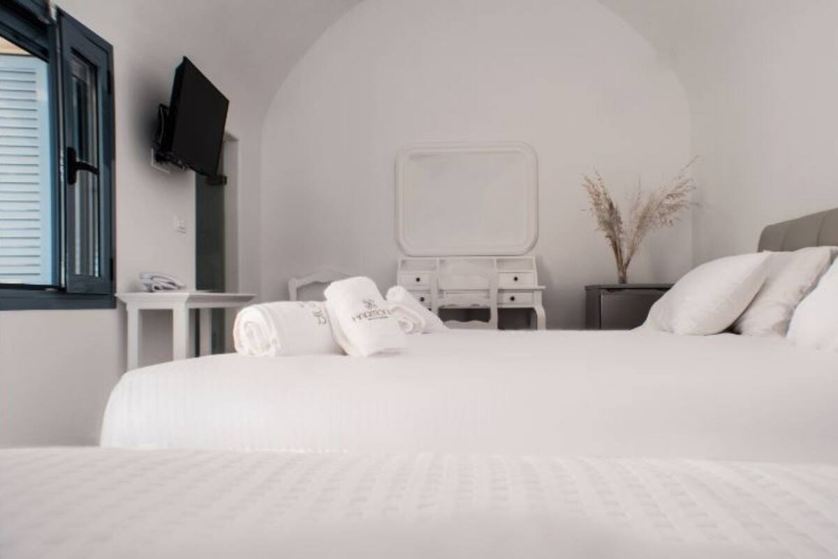 Quarto de hotel com uma cama grande, mesa de cabeceira, espelho, televisão fixada na parede e uma janela com persianas.