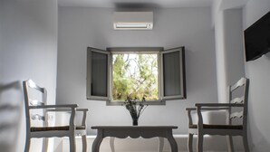 Une pièce avec deux chaises blanches, une petite table et une fenêtre dont les volets sont ouverts.