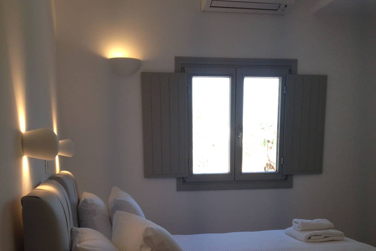 Quarto de hotel com duas camas, uma mesa de cabeceira com telefone e uma janela com persianas.