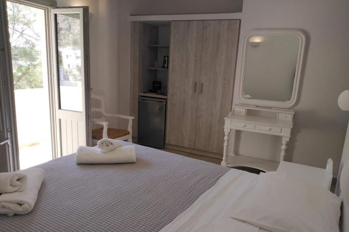 Quarto de hotel com uma cama grande, uma secretária pequena com espelho, um guarda-roupa e uma casa de banho.