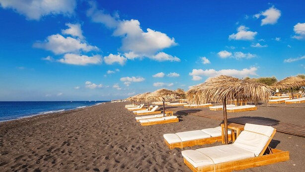 Une plage avec des transats et des parasols en chaume, un ciel dégagé et l’océan en toile de fond.