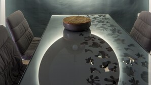 A modern dining area with a glass table, cushioned chairs, a round mirror, and pendant lighting. - apt27 (Nafplio)