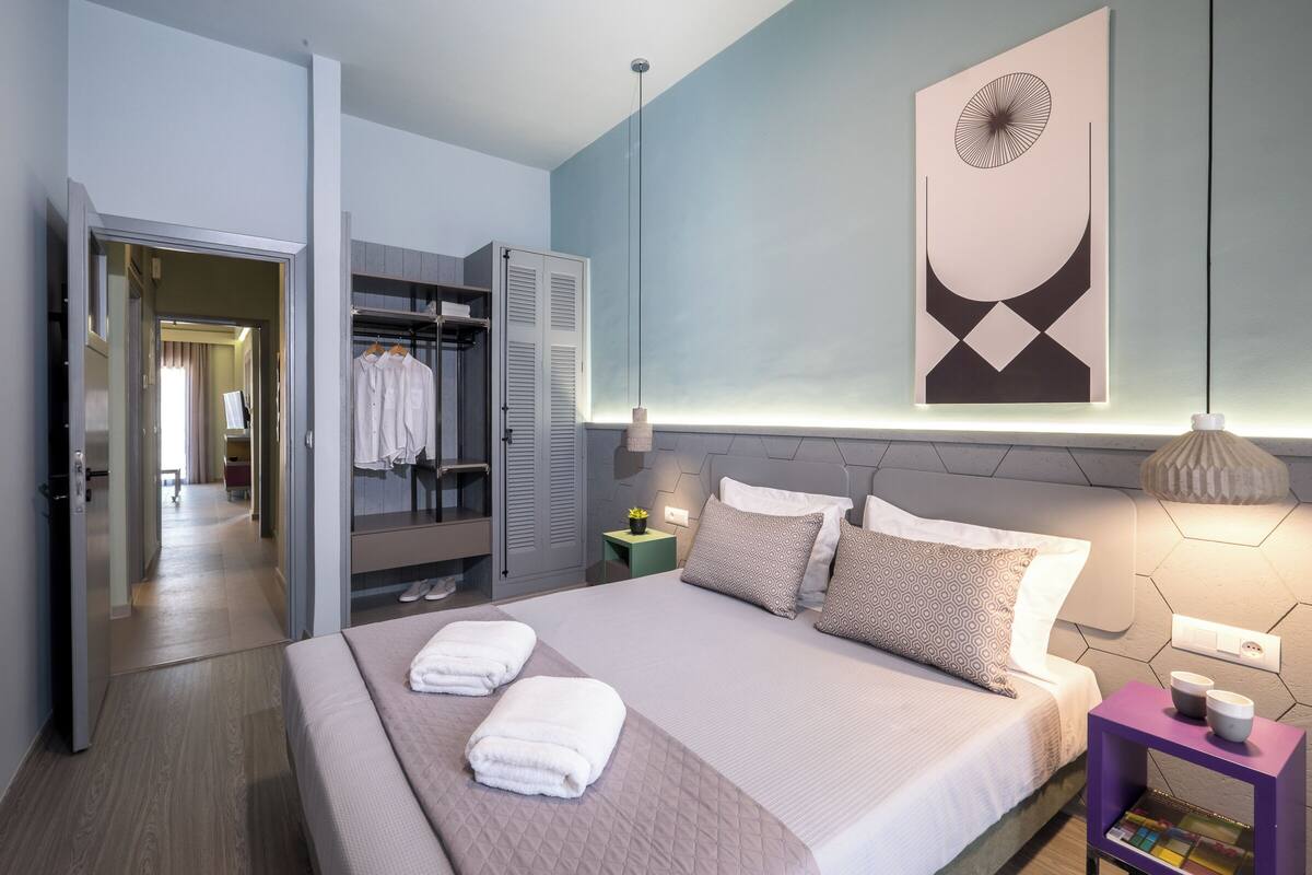 A modern hotel room with a neatly made bed, a walk-in closet, and a large abstract artwork on the wall.