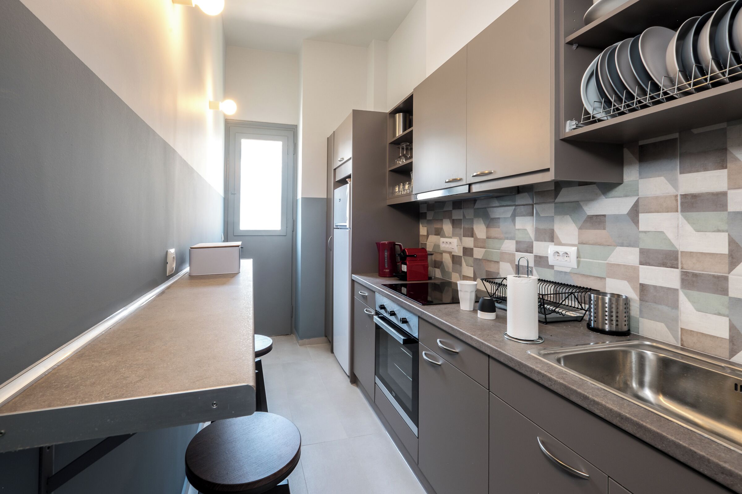 A modern kitchen with a built-in oven, stainless steel sink, and a tiled backsplash.