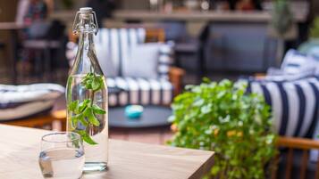 Une bouteille en verre transparent fermée par un fermoir en métal, un verre d’eau et une plante en pot, le tout posé sur une table en bois.