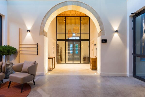 Un hall d’hôtel moderne avec une entrée en arc de cercle, un comptoir d’accueil et un espace détente agrémenté d’une plante en pot.