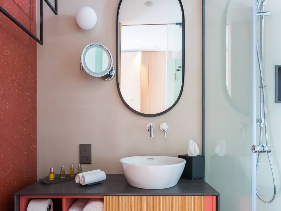 Ein modernes Badezimmer mit einem großen, ovalen Spiegel, einem weißen Waschbecken und einer Duschkabine aus Glas.