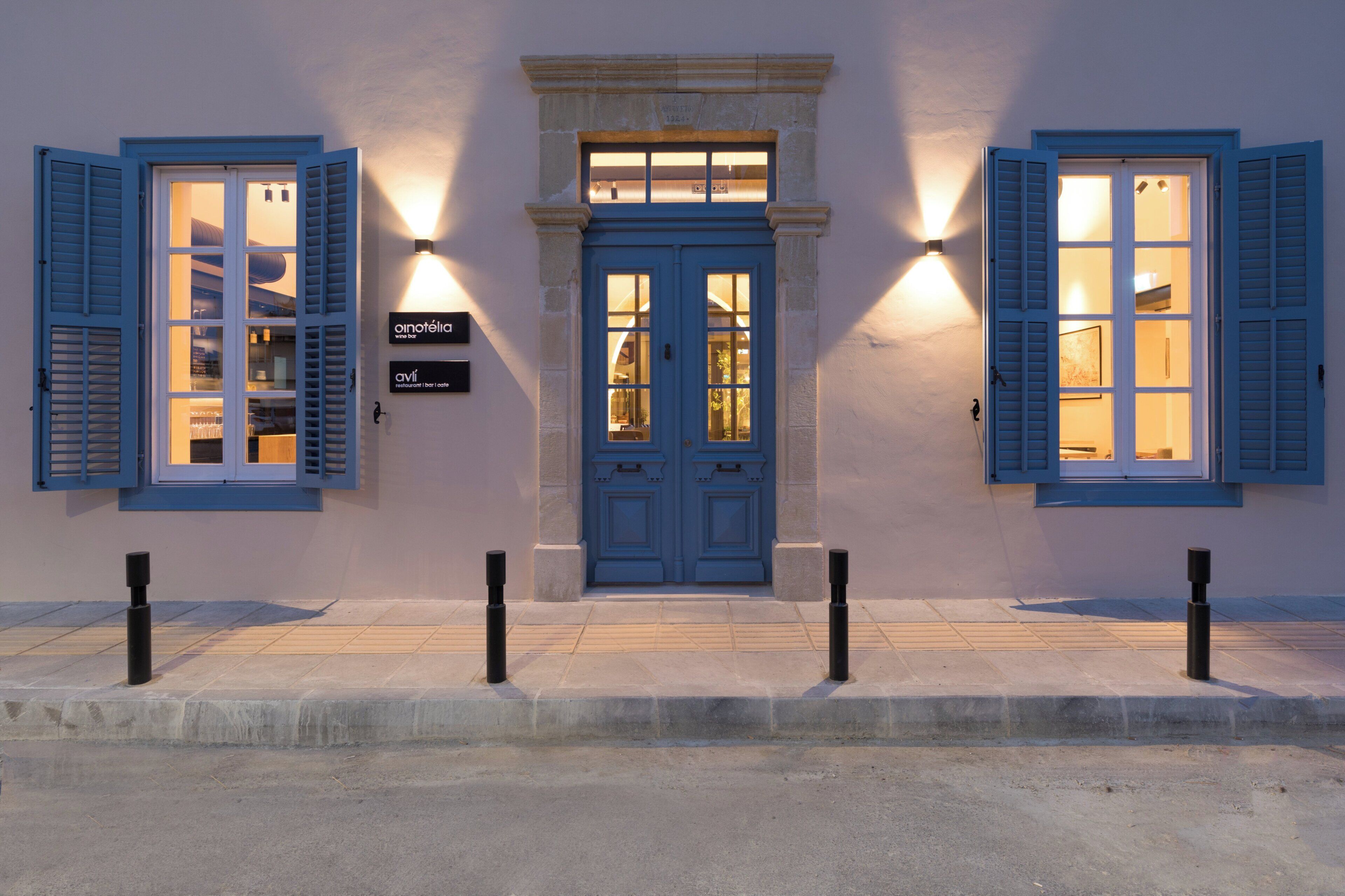 Un edificio con puerta y contraventanas azules, fachada de piedra y dos luces fijadas a la pared.