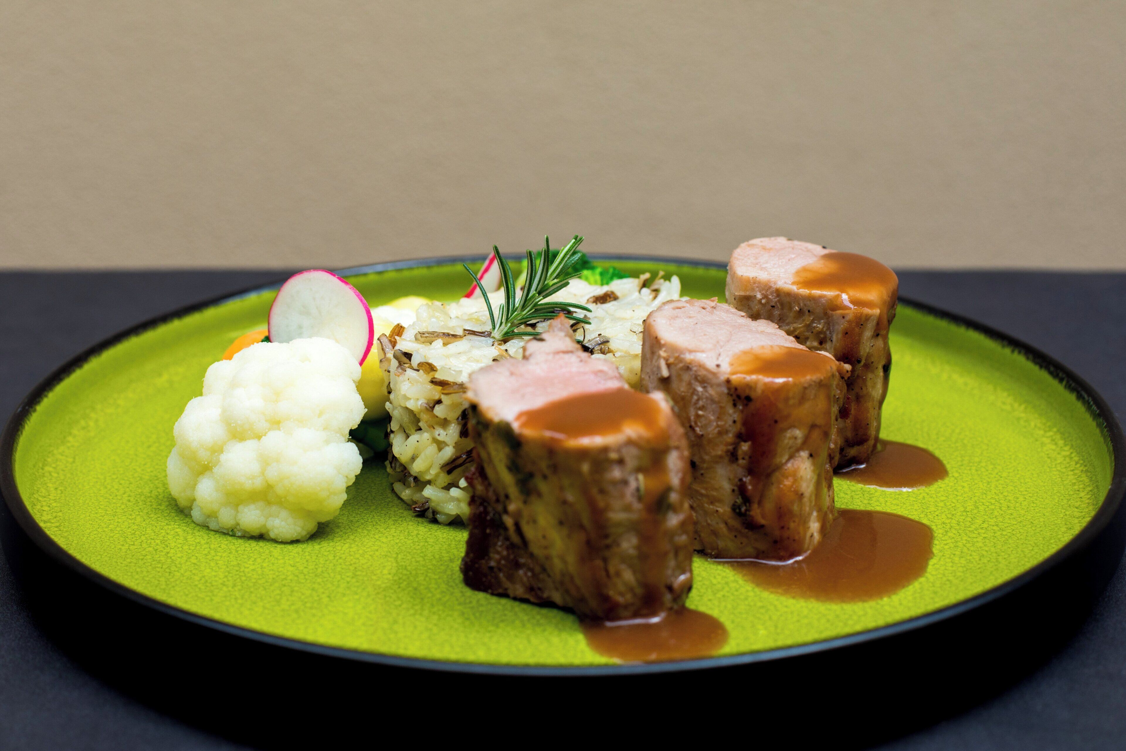 Un plato con alimentos, incluyendo coliflor, un trozo de carne con salsa y arroz.