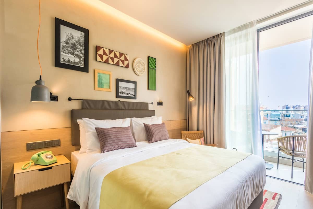 A hotel room with a large bed, a nightstand with a telephone, and a view of the city through the window.
