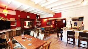 A cozy dining area with a wooden table and chairs, a television, and a bar area with a counter and various items. - The Nags Head (Thirsk)