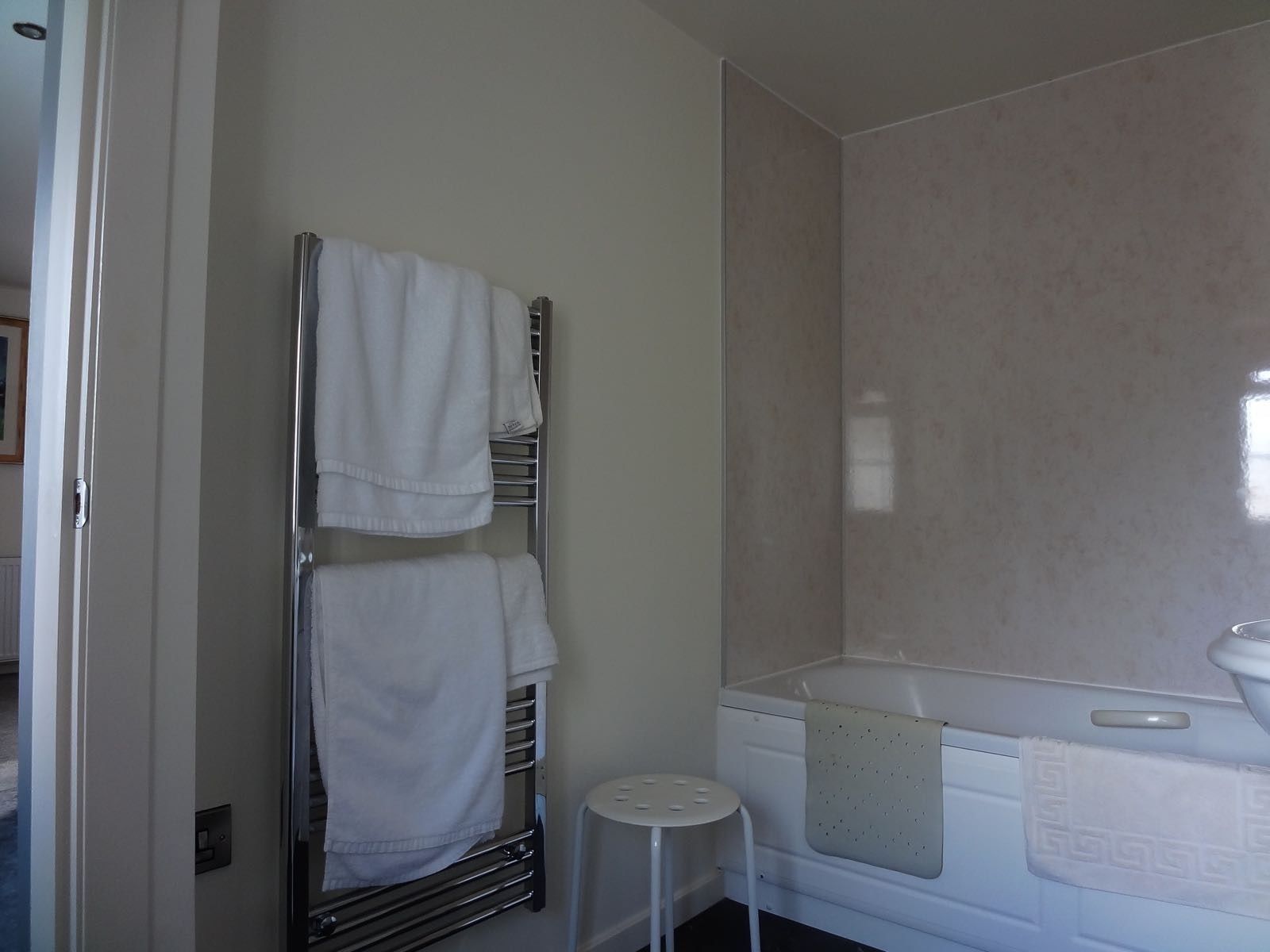 A bathroom with a white bathtub, a towel rack with two towels, and a small white stool.