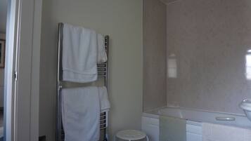 A bathroom with a white bathtub, a towel rack with two towels, and a small white stool.