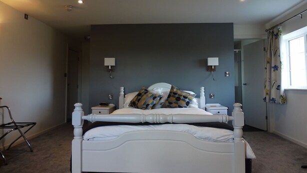 A bedroom with a double bed, two bedside tables, a chair, and a window with curtains. - The Nags Head (Thirsk)