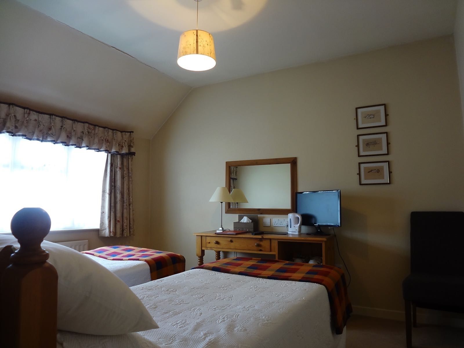 A hotel room with two beds, a desk with a computer, a chair, a lamp, and a window with curtains.