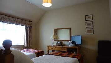 A hotel room with two beds, a desk with a computer, a chair, a lamp, and a window with curtains.