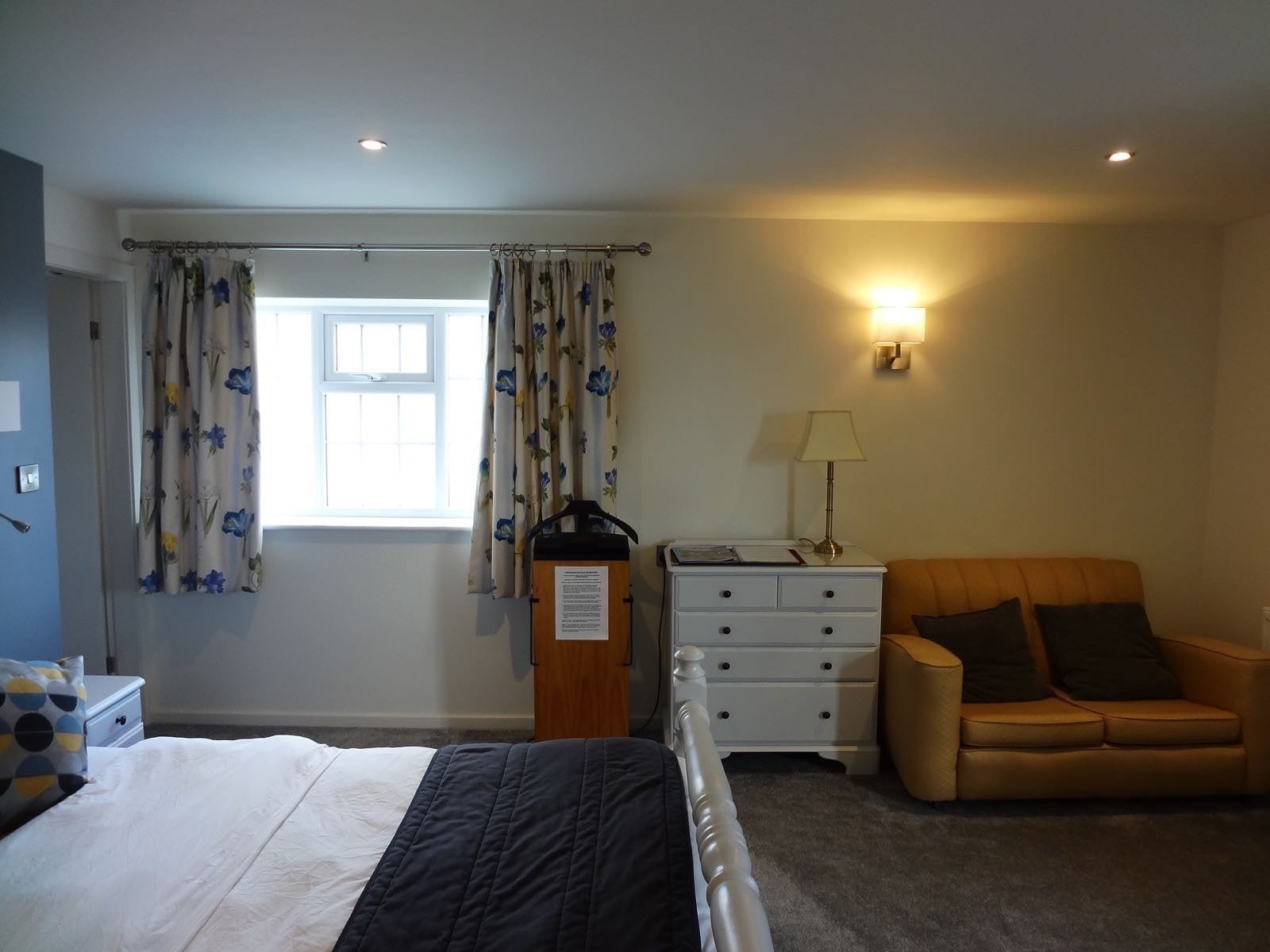 A bedroom with a bed, a nightstand, a lamp, a window with curtains, and a sofa.