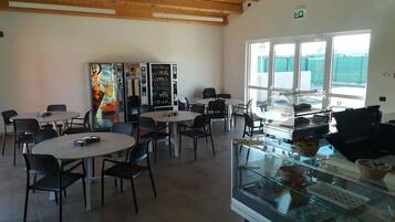 A café with round tables and black chairs, a vending machine, and a glass display case with pastries.