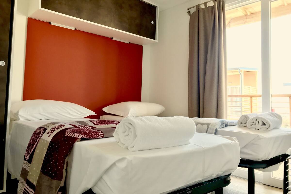 Une chambre d’hôtel avec deux lits, un mur d’accent de couleur rouge et une vue sur un bâtiment à l’extérieur.
