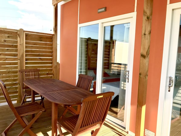 A wooden deck with a table and chairs, a sliding glass door leading to an interior space, and a wooden fence. - Camping Verona Village (Verona)