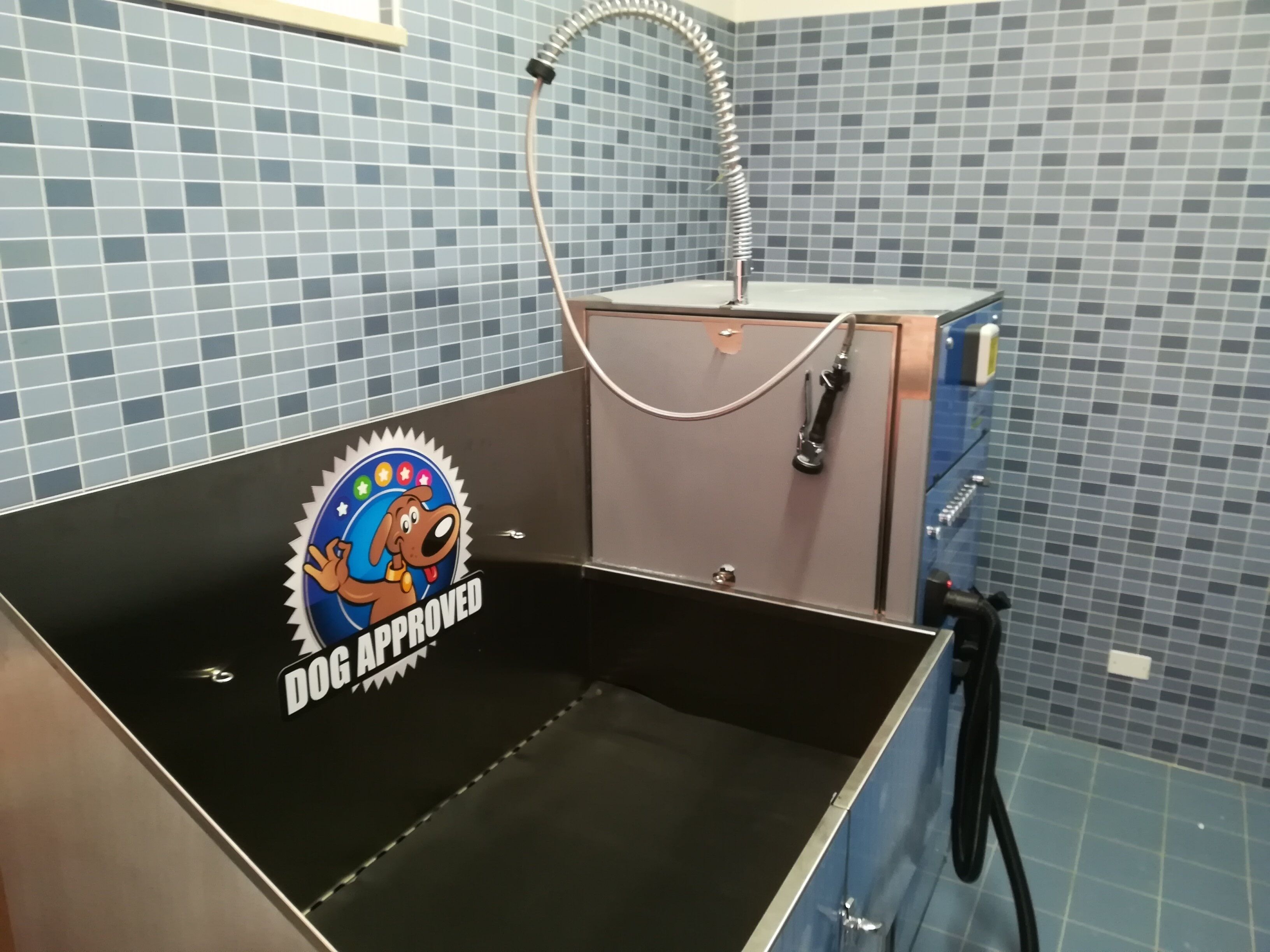 A grooming station with a blue tiled wall, a metal sink, and a dog approval sticker.