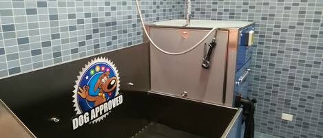 A grooming station with a blue tiled wall, a metal sink, and a dog approval sticker.