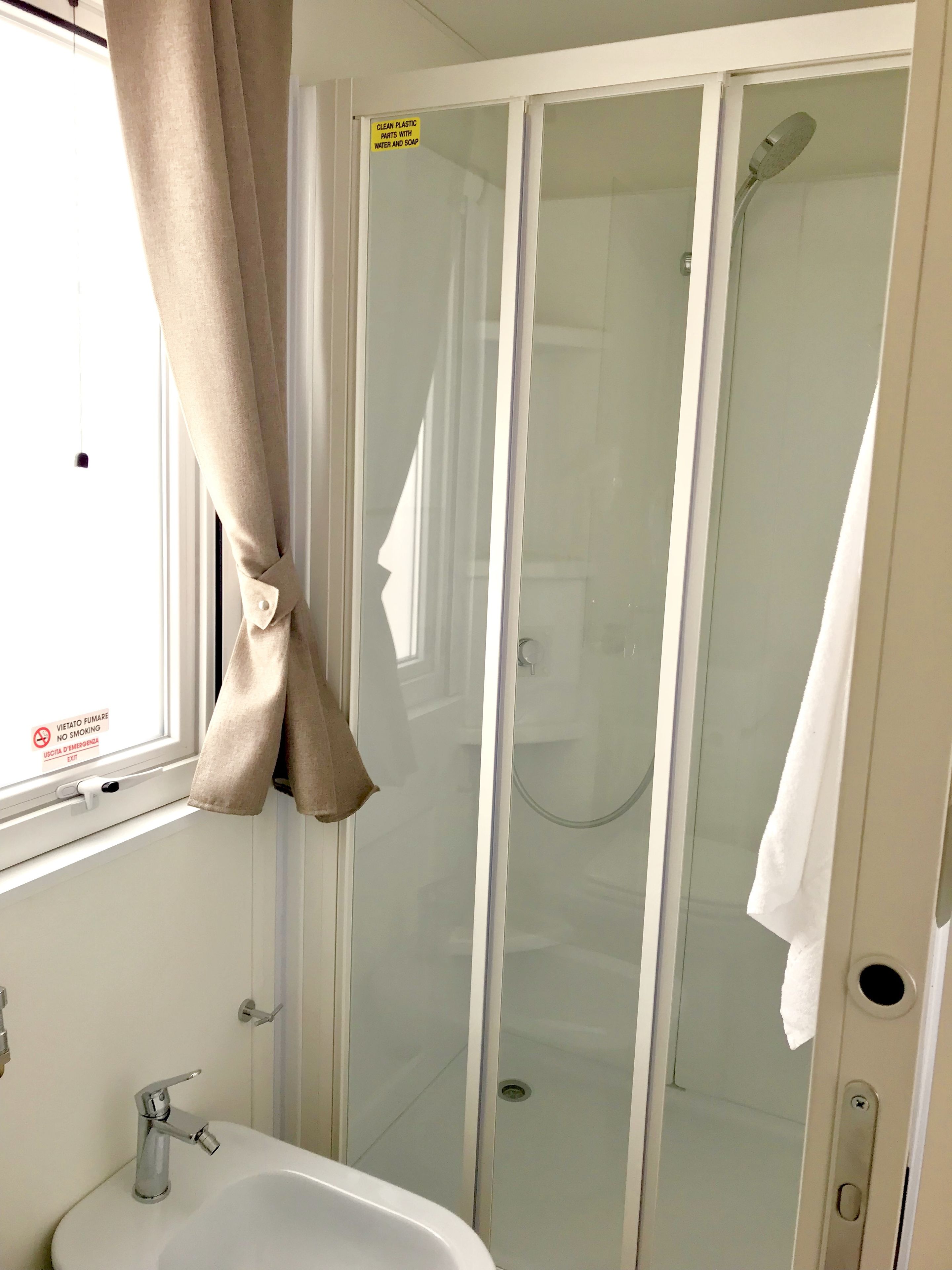 A bathroom with a glass shower enclosure, a sink, and a window with curtains.