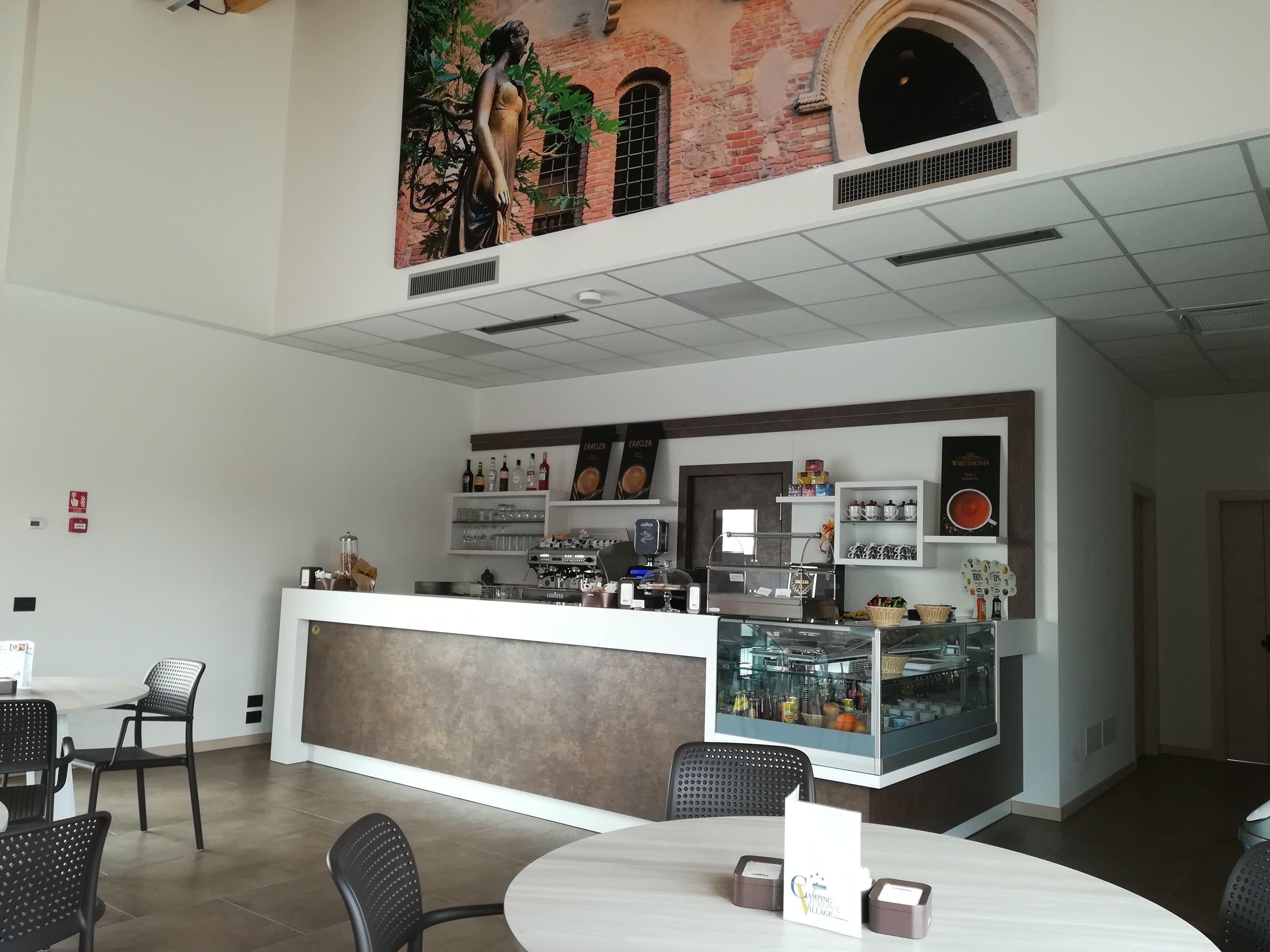 A modern cafe with a counter, seating area, and a mural on the wall.
