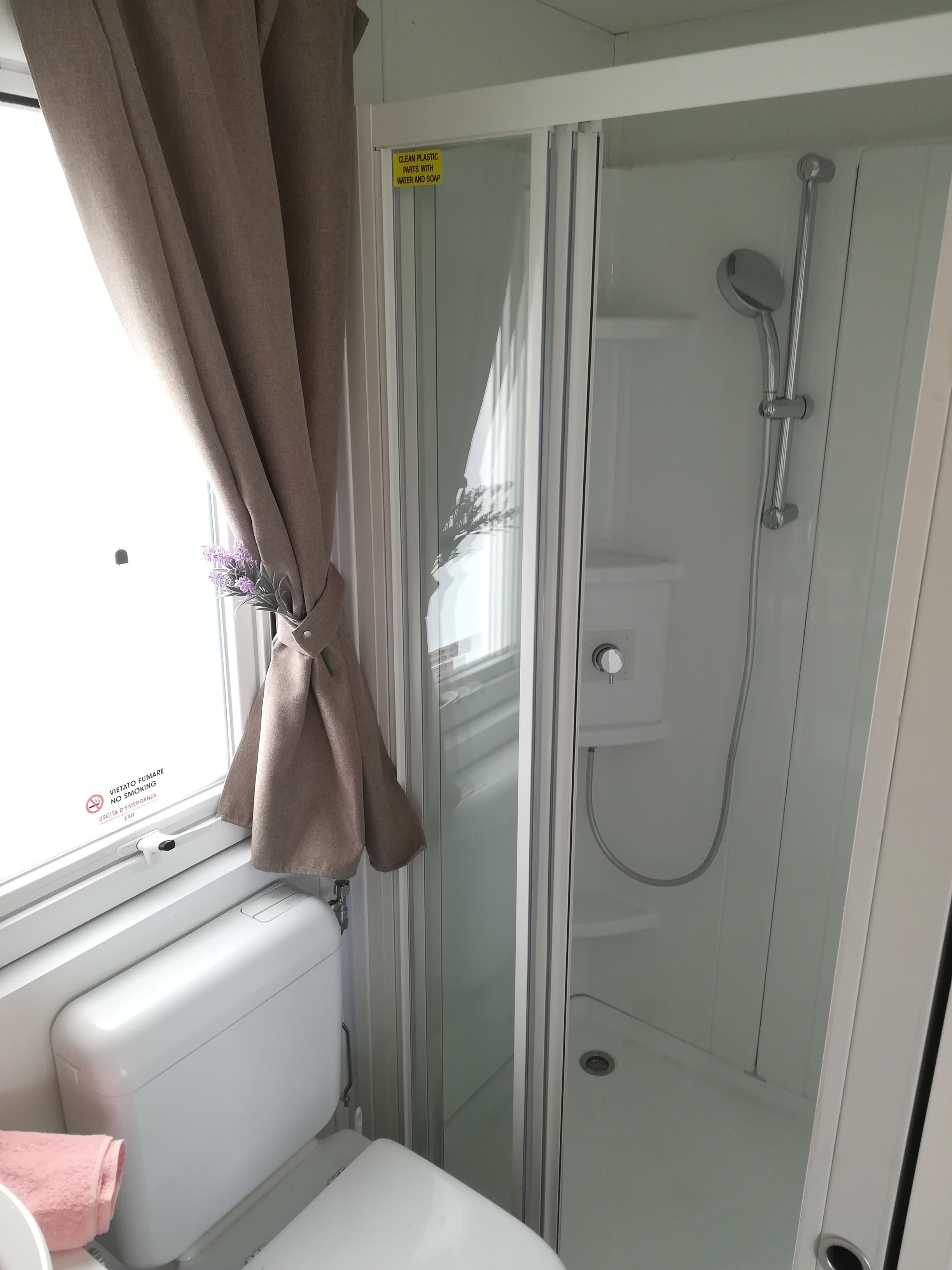 A bathroom with a glass shower enclosure, a towel rack, and a window with curtains.
