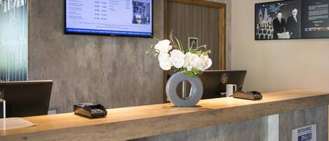 Un mostrador de recepción con un monitor que muestra un presupuesto, un florero con flores blancas y un letrero sobre el saldo de registro.