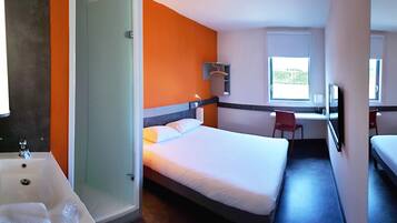 A hotel room with a bed, a desk, a chair, and a bathroom with a bathtub and sink.