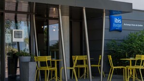 A modern building with a sign for 'Ibis Budget' and outdoor seating with yellow chairs. - ibis budget Archamps Porte de Genève (Archamps)