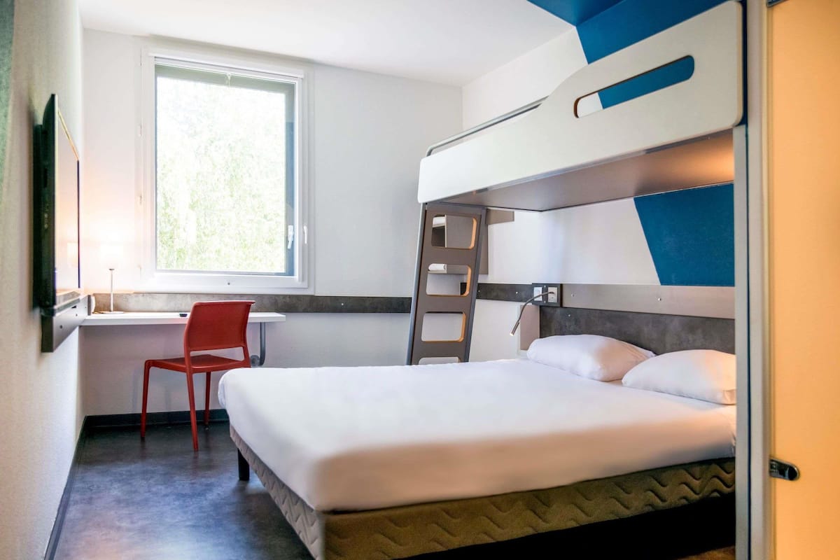 Habitación con literas, un escritorio, una silla, una ventana con vistas y una escalera.