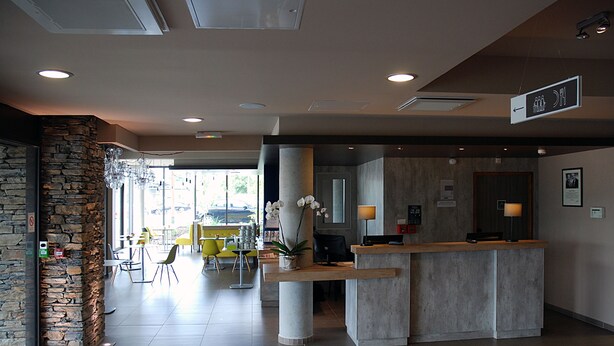 A reception area with a stone wall, a reception desk, and a seating area with yellow chairs. - ibis budget Archamps Porte de Genève (Archamps)