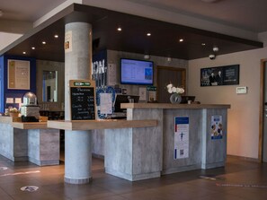 A reception area with a counter, a computer monitor, a chalkboard menu, and a security camera. - ibis budget Archamps Porte de Genève (Archamps)