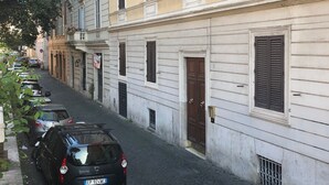 A narrow cobblestone street lined with multi-story buildings, parked cars, and a tree. - Art Atelier Vaticano (Rome)
