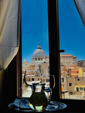 A view of a cityscape through a window with a table featuring a glass pitcher and a plate. - Art Atelier Vaticano (Rome)