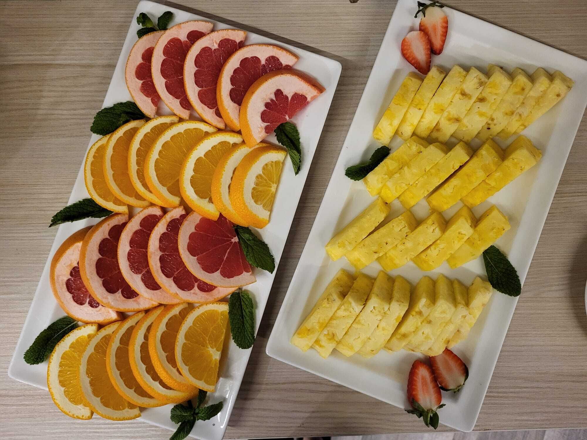 Two rectangular white plates with sliced fruits and a strawberry.