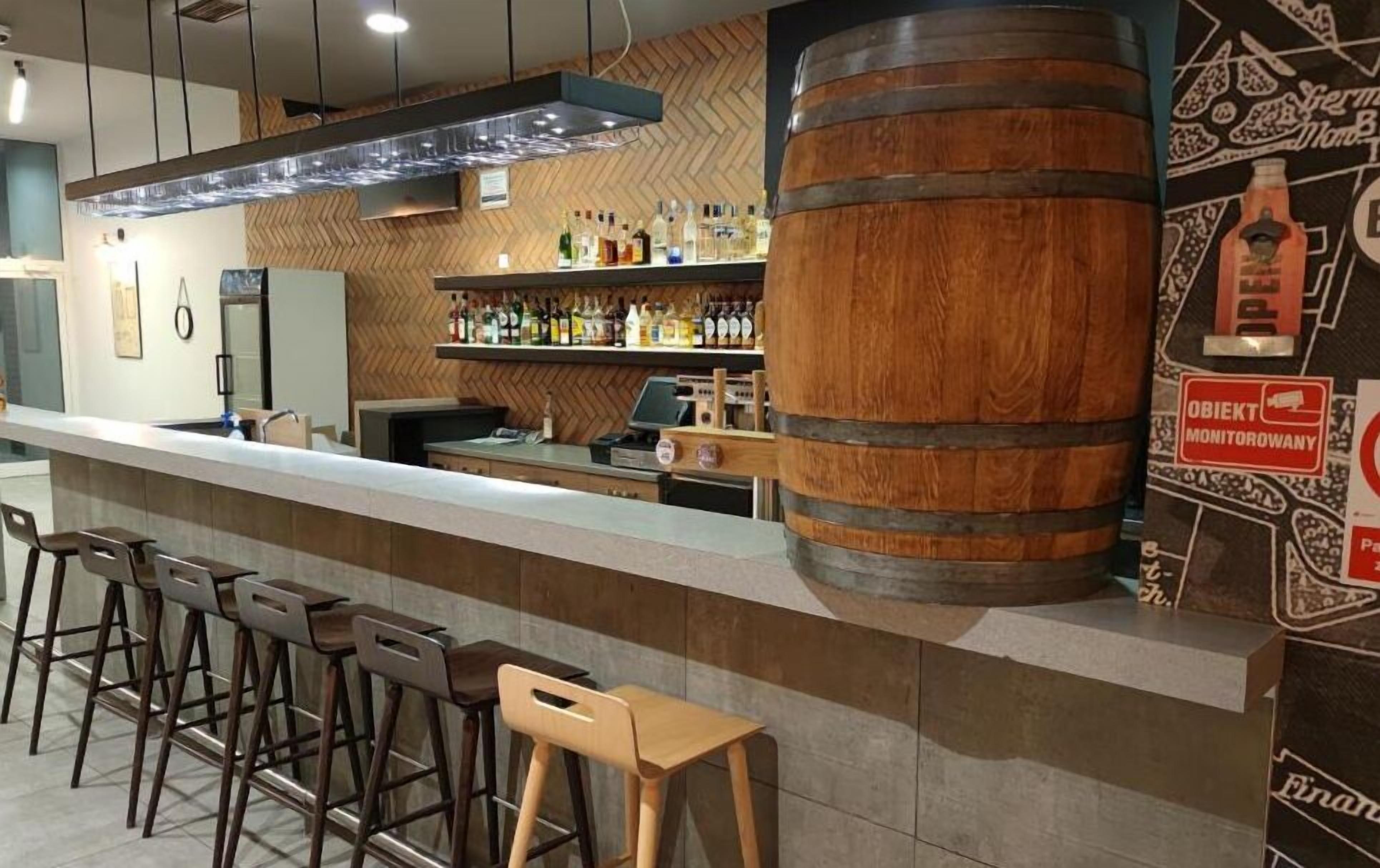 A bar area with stools, a wooden barrel, and shelves of bottles.
