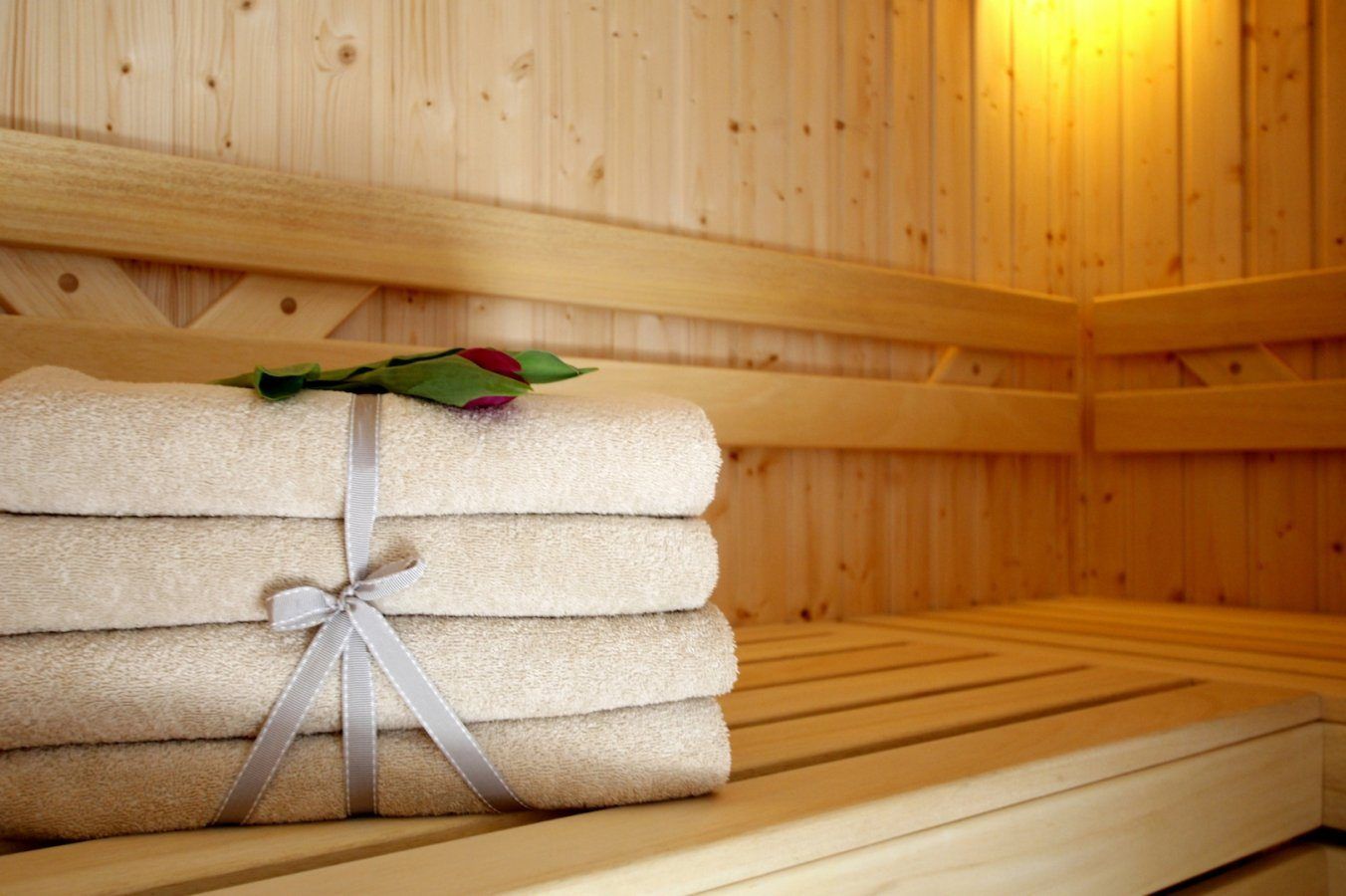 Una pila de toallas dobladas con cuidado atadas con un lazo, sobre un banco de madera en una habitación de madera con techo de listones.